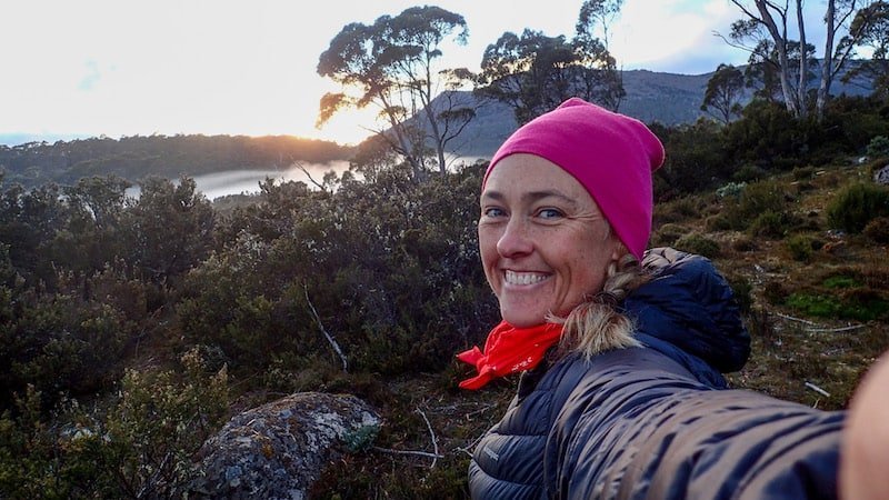 female hiker with pink beanie smiles to camera with misty scene behind